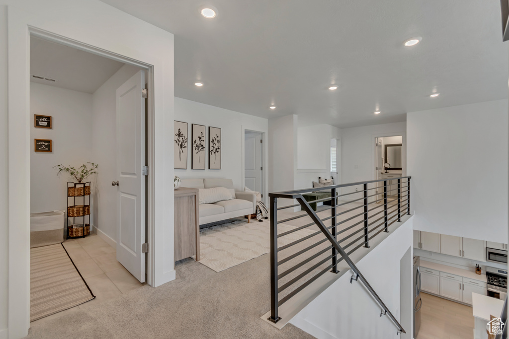 Corridor with an upstairs landing, recessed lighting, and light carpet