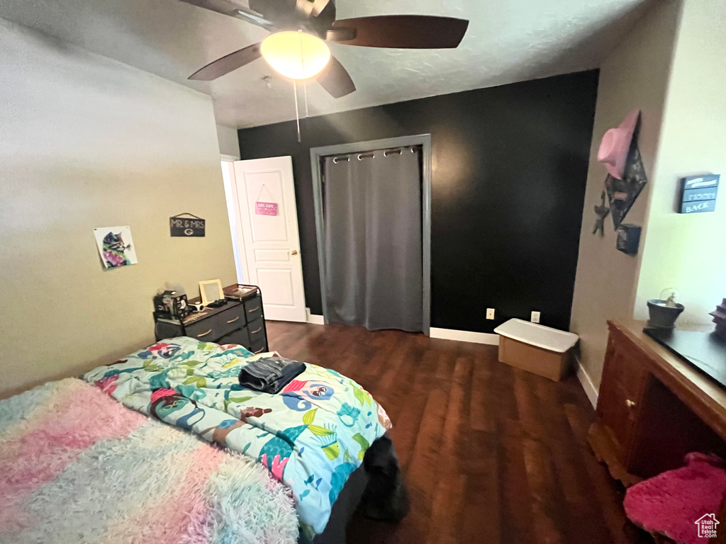 Bedroom with dark wood-style floors, ceiling fan, baseboards, and a closet