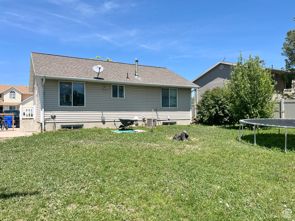 Rear view of property with a trampoline and a yard