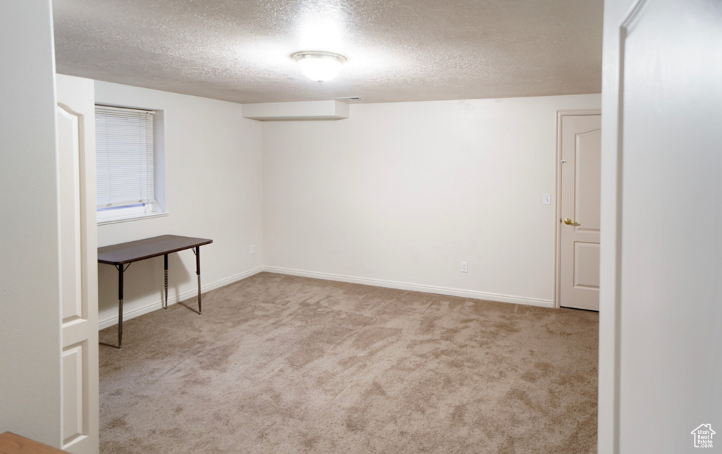 Empty room with a textured ceiling, carpet, and baseboards