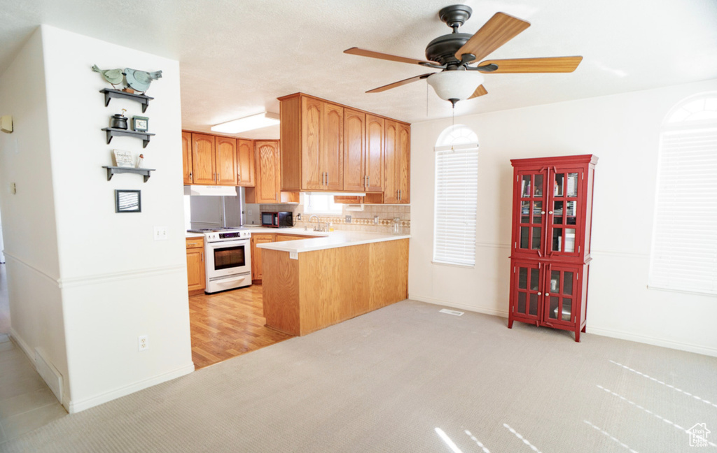 Kitchen with electric stove, black microwave, a peninsula, light countertops, and ceiling fan