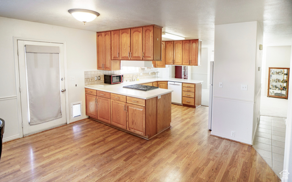 Kitchen with white appliances, a peninsula, light wood finished floors, light countertops, and tasteful backsplash