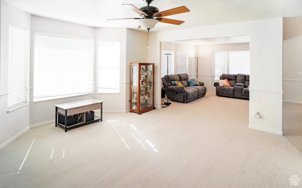 Carpeted living room featuring a ceiling fan and baseboards