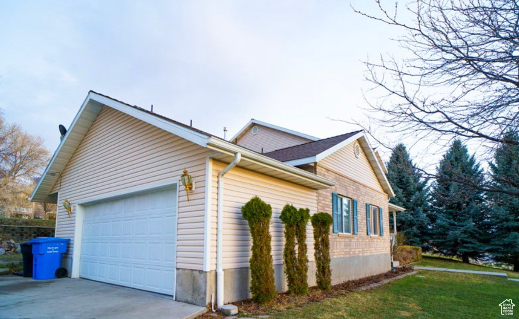 View of property exterior featuring an attached garage, driveway, and a lawn
