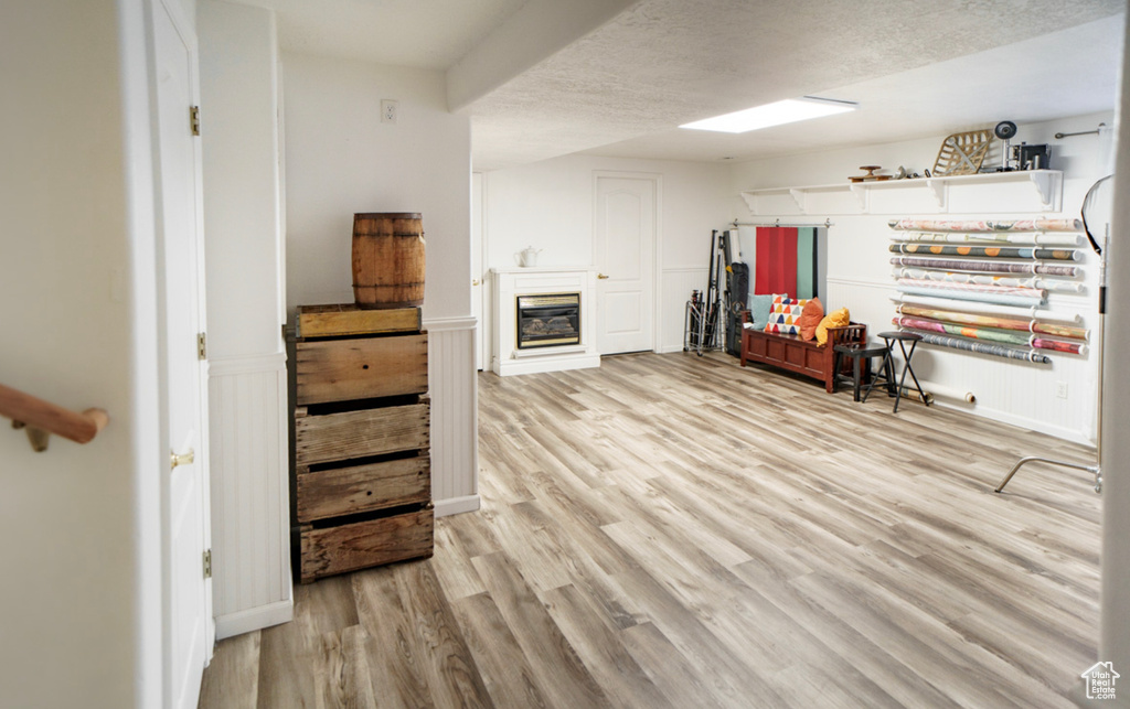 Basement featuring light wood finished floors, a wainscoted wall, a glass covered fireplace, and a textured ceiling