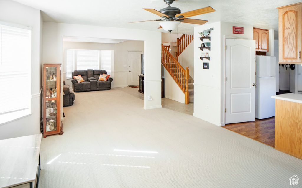 Carpeted living room with ceiling fan, stairway, and baseboards