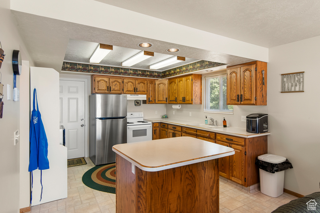 Kitchen featuring freestanding refrigerator, white electric range oven, a sink, under cabinet range hood, and brown cabinets