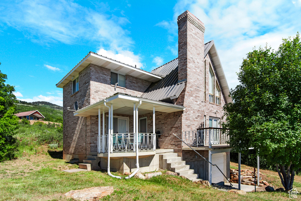 Rear view of property with covered porch, a chimney, metal roof, a garage, and brick siding