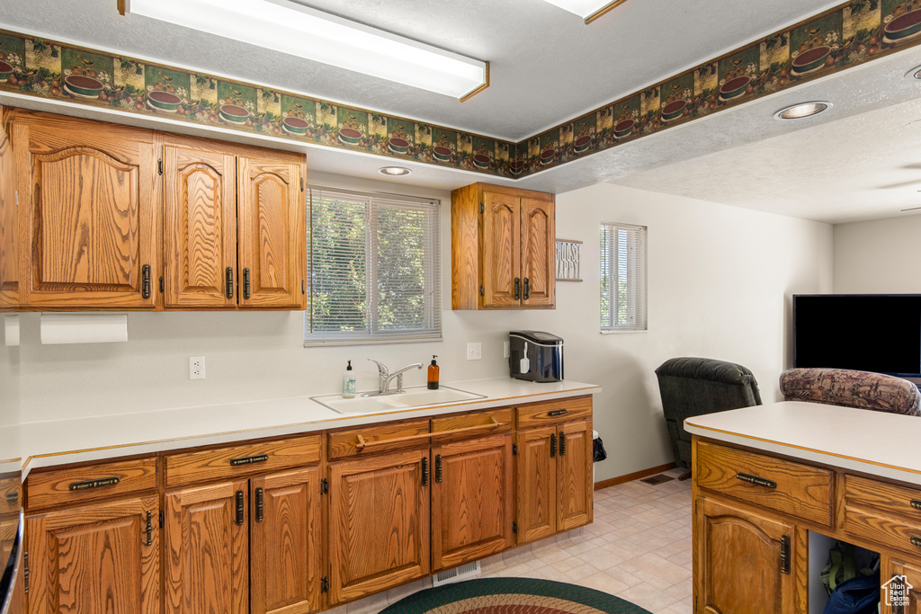 Kitchen featuring a sink, light countertops, open floor plan, and brown cabinetry