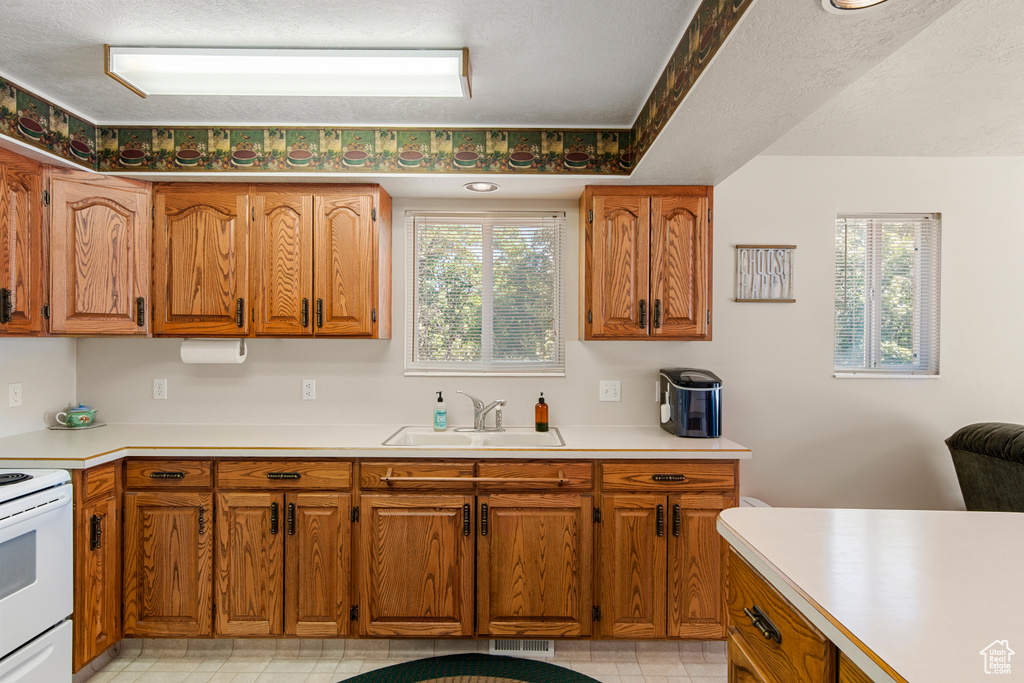 Kitchen featuring a sink, white electric stove, brown cabinets, and light countertops