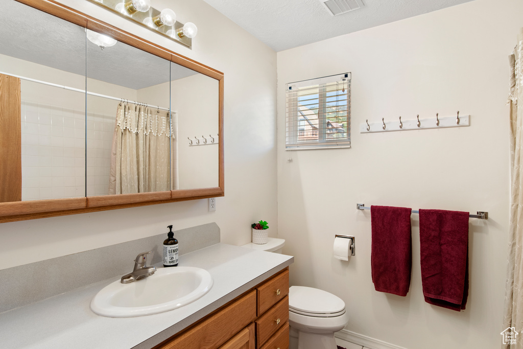Bathroom with toilet, vanity, and curtained shower