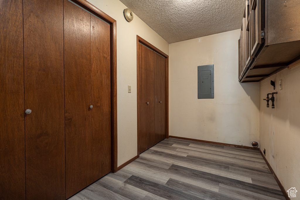 Hallway with wood finished floors, electric panel, a textured ceiling, and baseboards