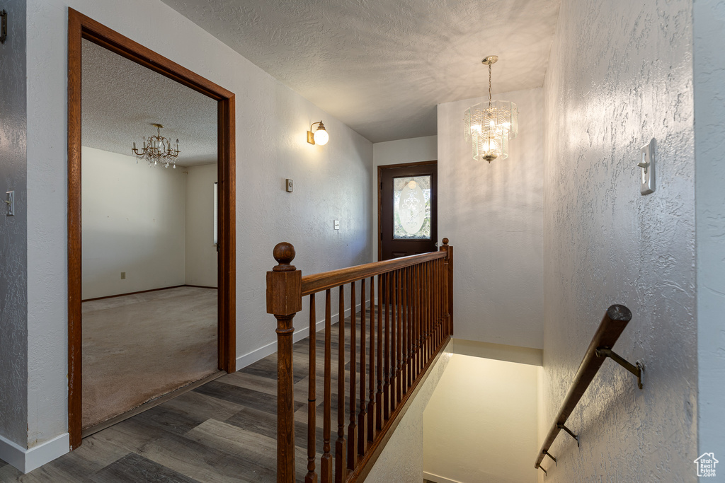 Stairway with a chandelier, wood finished floors, a textured ceiling, a textured wall, and baseboards