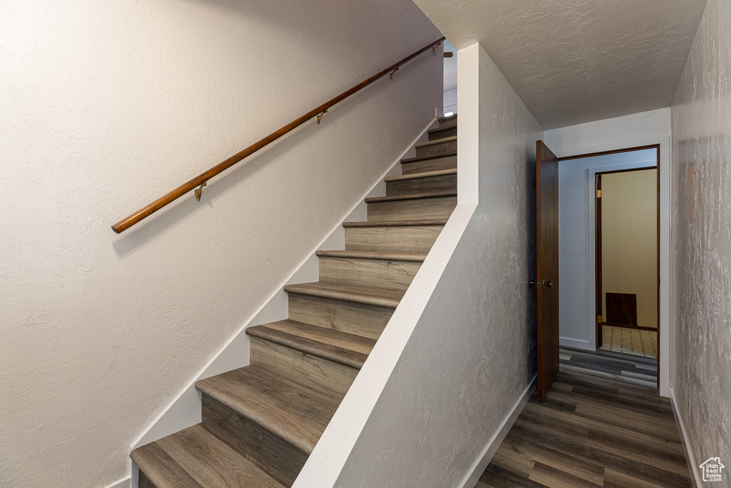 Stairway featuring baseboards, wood finished floors, a textured wall, and a textured ceiling