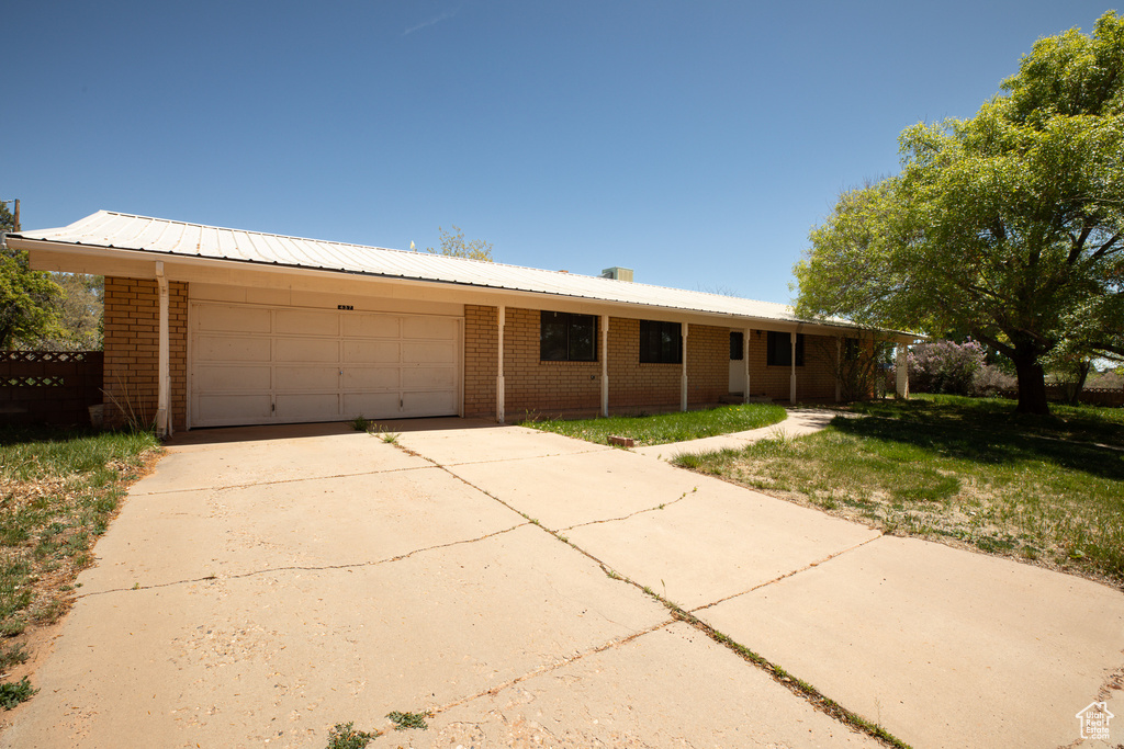 Single story home featuring brick siding, a garage, concrete driveway, and metal roof
