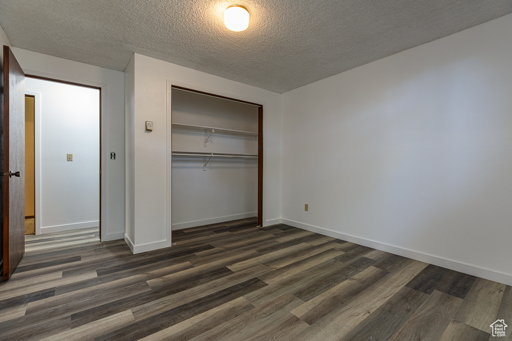 Unfurnished bedroom with a textured ceiling, a closet, dark wood-style flooring, and baseboards