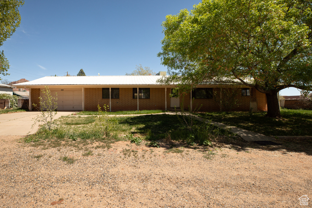 Single story home featuring an attached garage, brick siding, concrete driveway, and metal roof