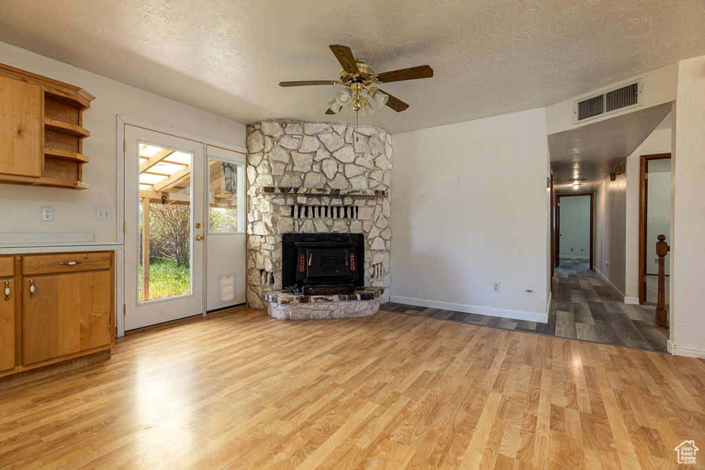 Unfurnished living room with light wood-style flooring, a ceiling fan, a textured ceiling, a fireplace, and baseboards