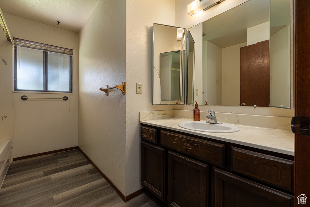 Bathroom with wood finished floors, vanity, baseboards, and a bath