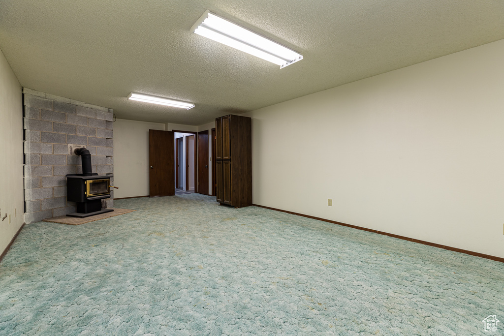 Unfurnished living room with a wood stove, a textured ceiling, and light colored carpet