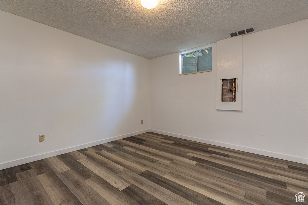 Empty room with dark wood-type flooring, a textured ceiling, and baseboards