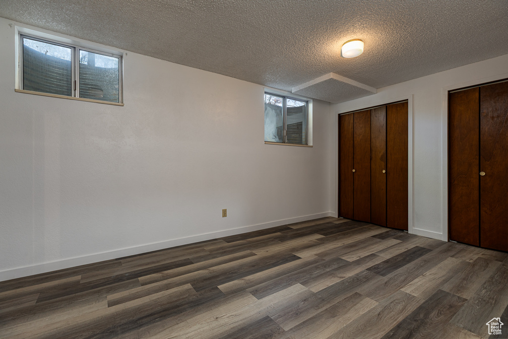 Unfurnished bedroom featuring a textured ceiling, dark wood finished floors, two closets, and baseboards