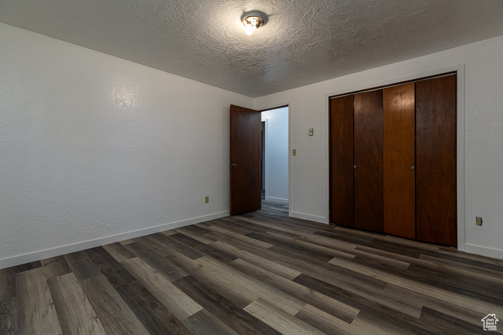 Unfurnished bedroom featuring dark wood finished floors, baseboards, a closet, and a textured ceiling