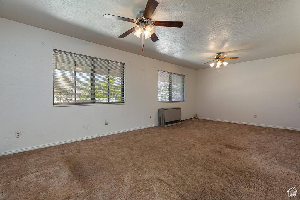 Carpeted spare room featuring a textured ceiling, a ceiling fan, baseboards, and heating unit
