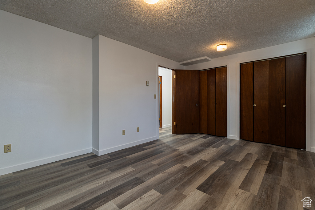 Unfurnished bedroom featuring a textured ceiling, dark wood-type flooring, multiple closets, and baseboards