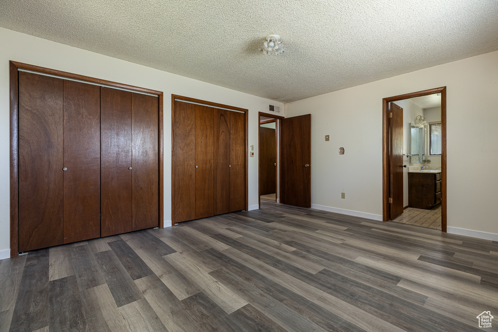 Unfurnished bedroom featuring two closets, dark wood-type flooring, a textured ceiling, connected bathroom, and baseboards