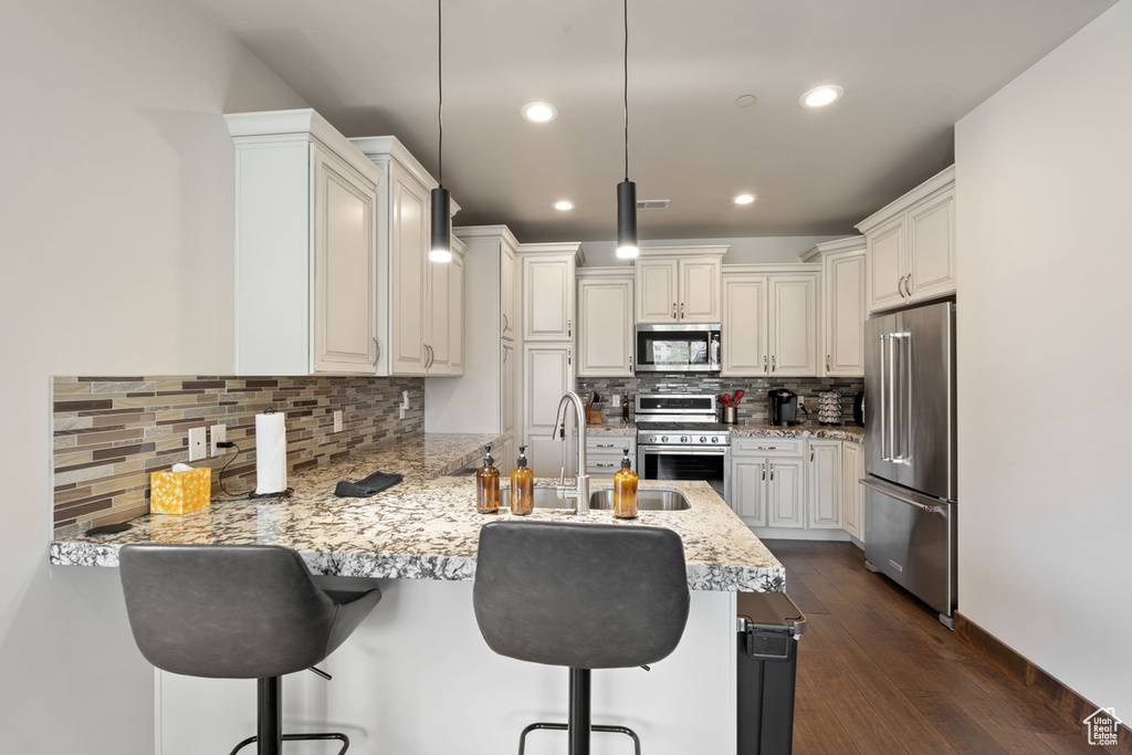 Kitchen with appliances with stainless steel finishes, a peninsula, a breakfast bar area, decorative backsplash, and recessed lighting