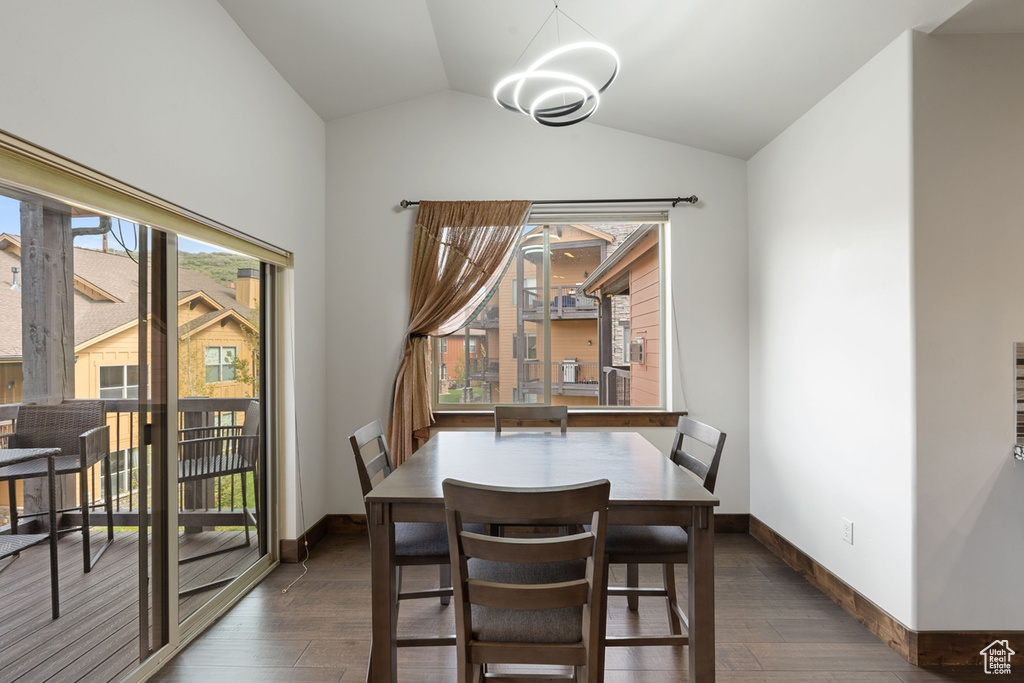 Dining space with dark wood-style floors, lofted ceiling, baseboards, and a chandelier