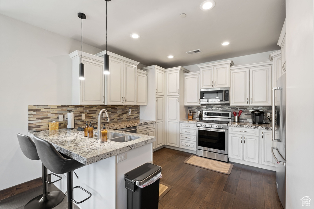 Kitchen featuring appliances with stainless steel finishes, a peninsula, a sink, tasteful backsplash, and a breakfast bar area