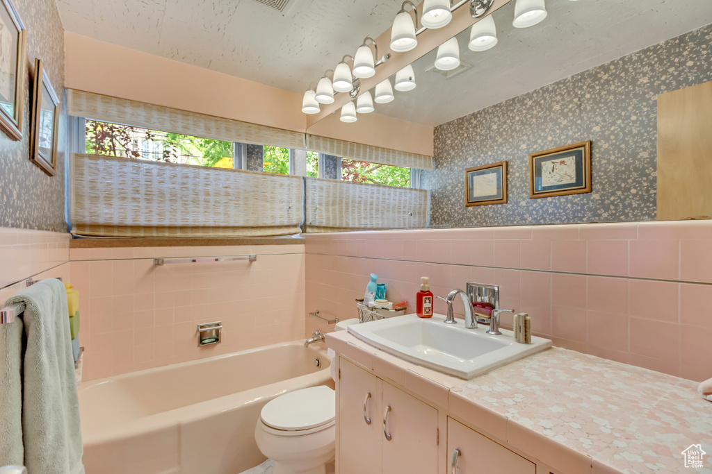 Bathroom featuring wallpapered walls, a bath, tile walls, vanity, and toilet