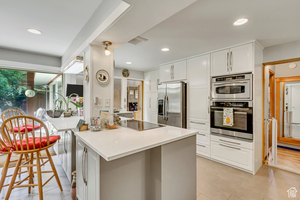 Kitchen featuring stainless steel appliances, white cabinetry, a peninsula, light tile patterned floors, and light countertops