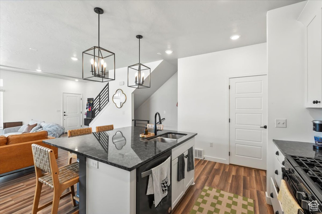 Kitchen featuring a sink, black dishwasher, dark wood-type flooring, a breakfast bar area, and dark stone counters