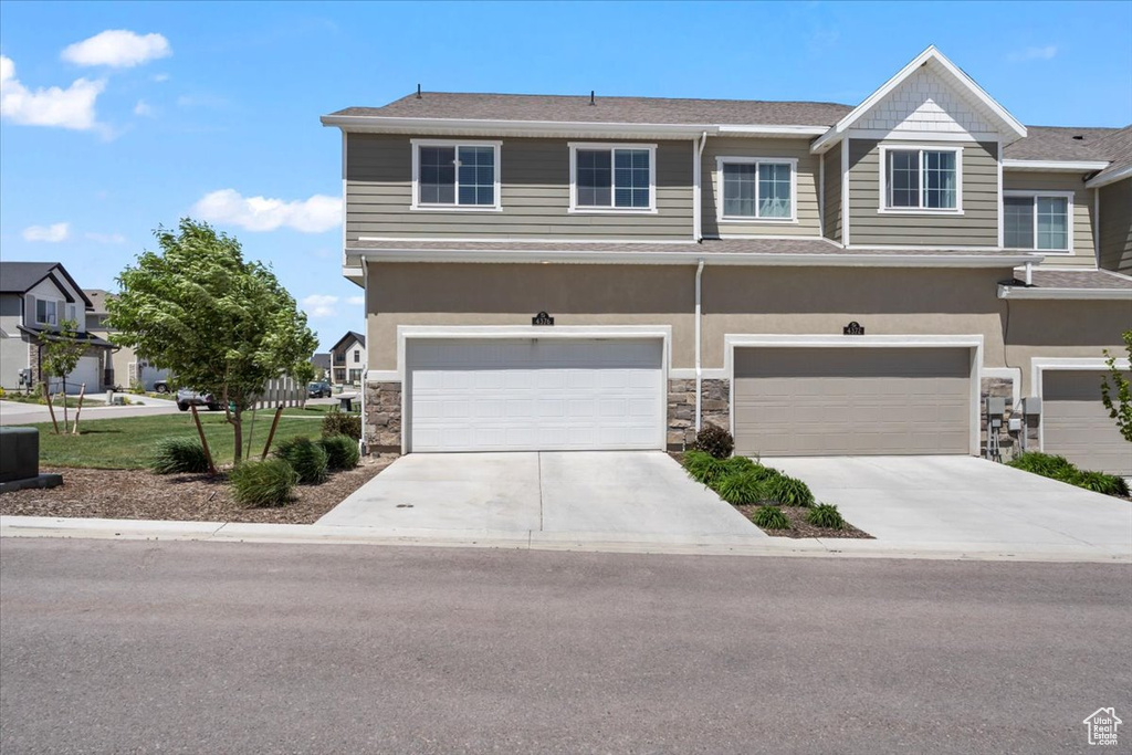 View of front facade featuring driveway, stone siding, a garage, and stucco siding