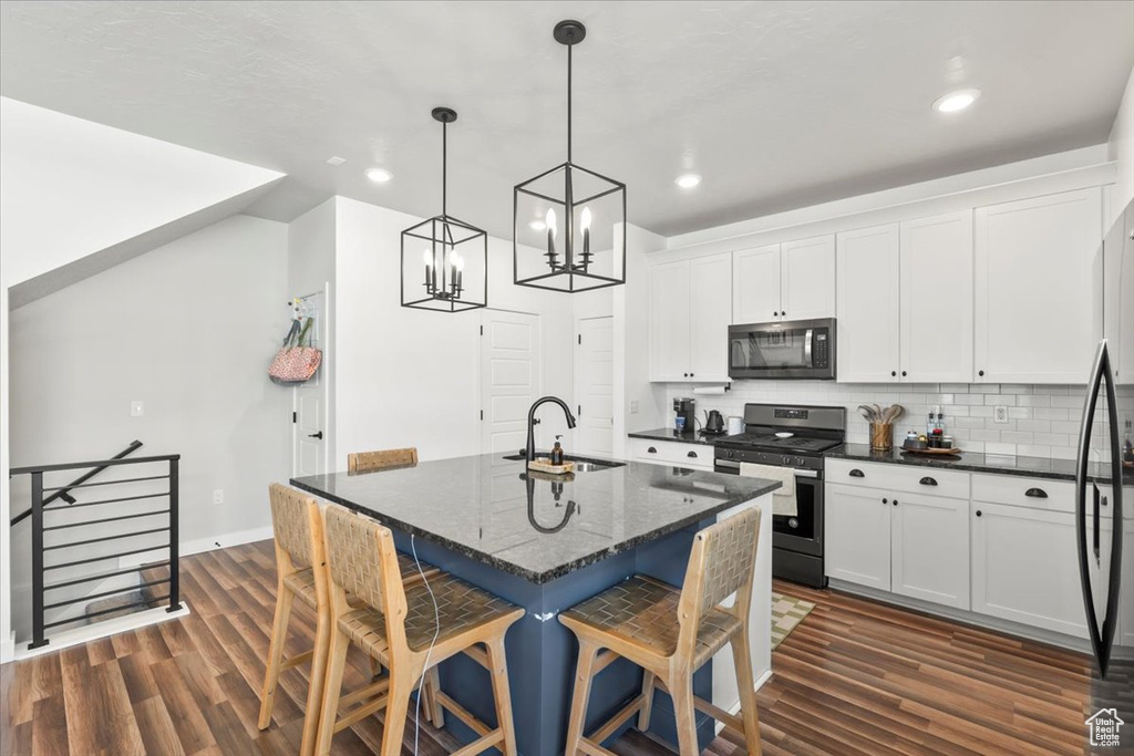 Kitchen featuring appliances with stainless steel finishes, a sink, a kitchen breakfast bar, white cabinetry, and backsplash