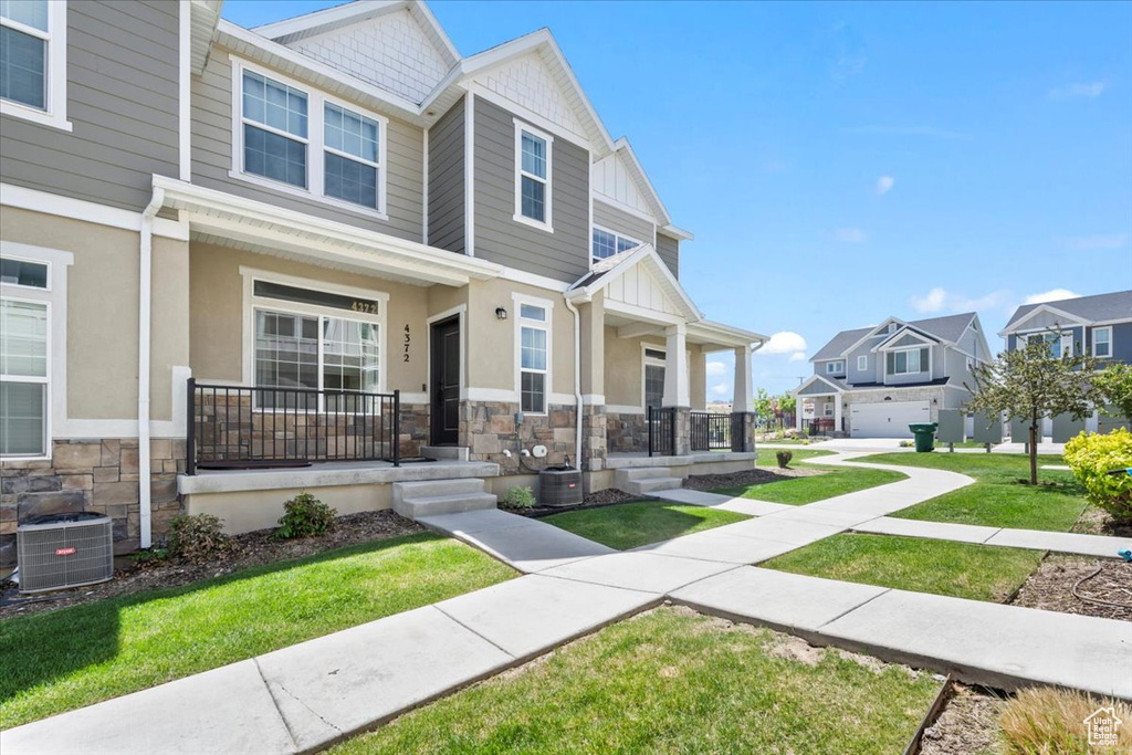 View of front of home with covered porch, stone siding, central AC unit, and a residential view