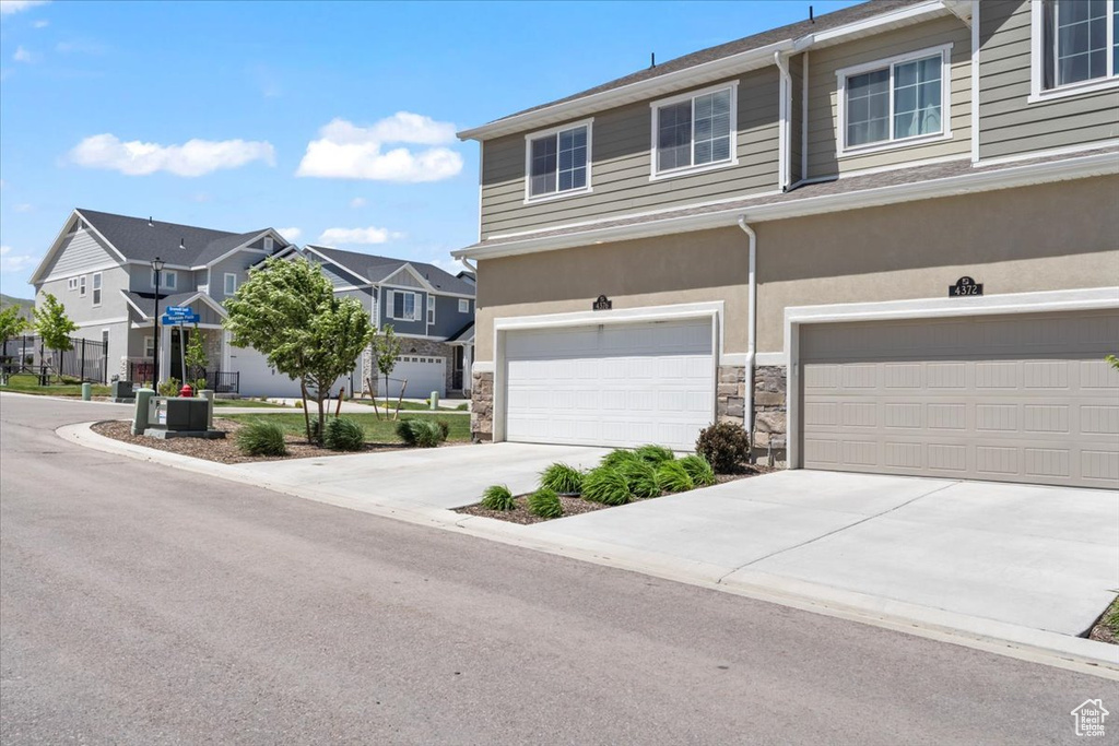 Multi unit property featuring a residential view, stone siding, driveway, and an attached garage