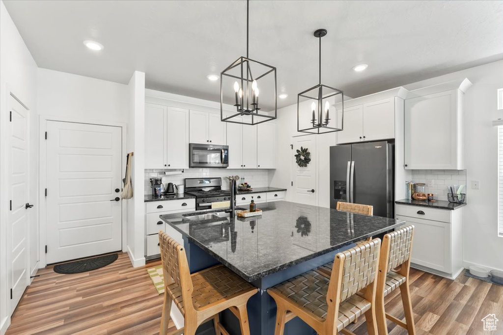 Kitchen featuring stainless steel appliances, light wood finished floors, decorative backsplash, a kitchen breakfast bar, and a chandelier