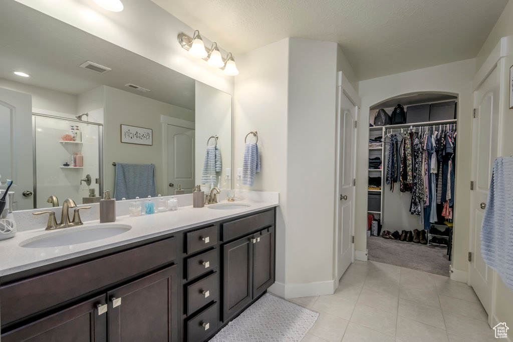 Bathroom with baseboards, a shower stall, double vanity, and tile patterned floors