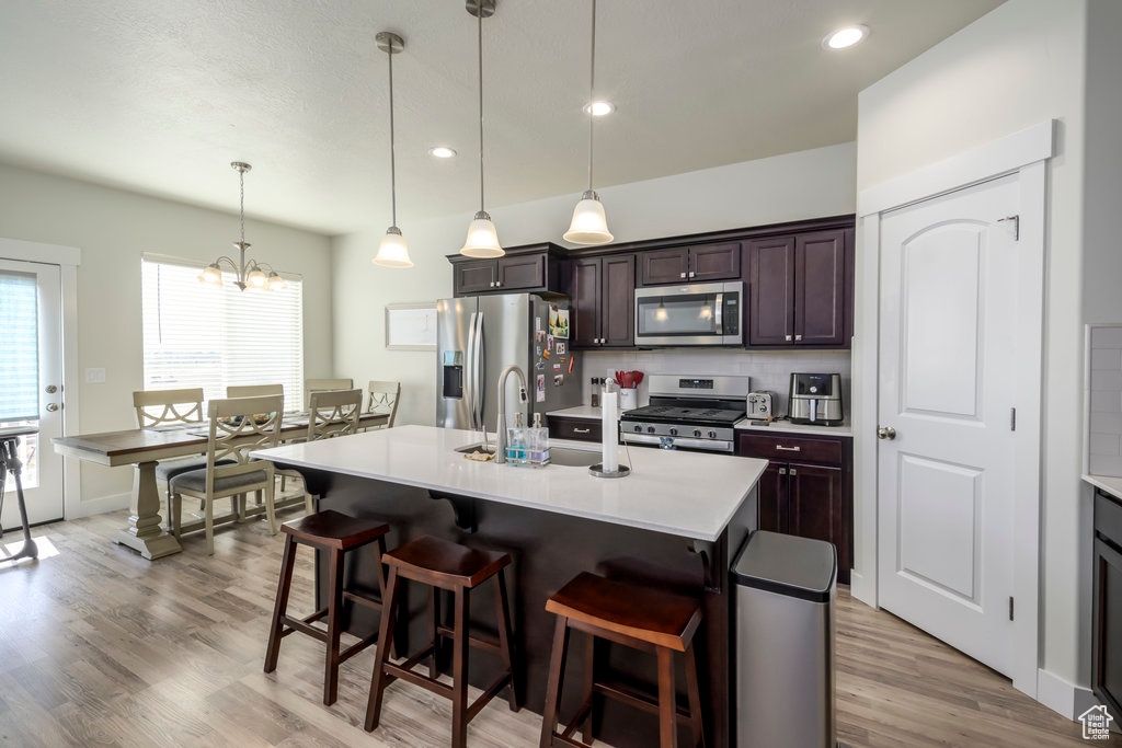 Kitchen featuring stainless steel appliances, a kitchen bar, light countertops, light wood-type flooring, and a center island with sink