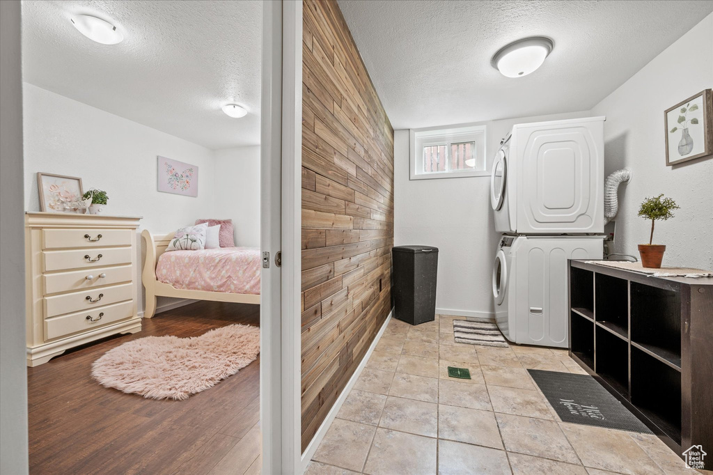 Laundry area featuring stacked washing machine and dryer, a textured ceiling, wooden walls, and baseboards