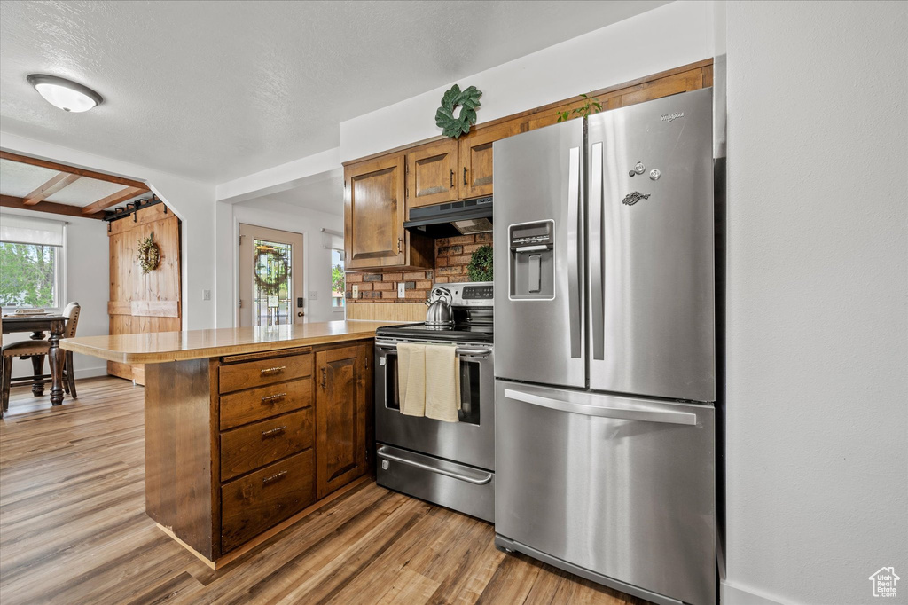 Kitchen with stainless steel appliances, a peninsula, under cabinet range hood, brown cabinets, and light wood-style flooring