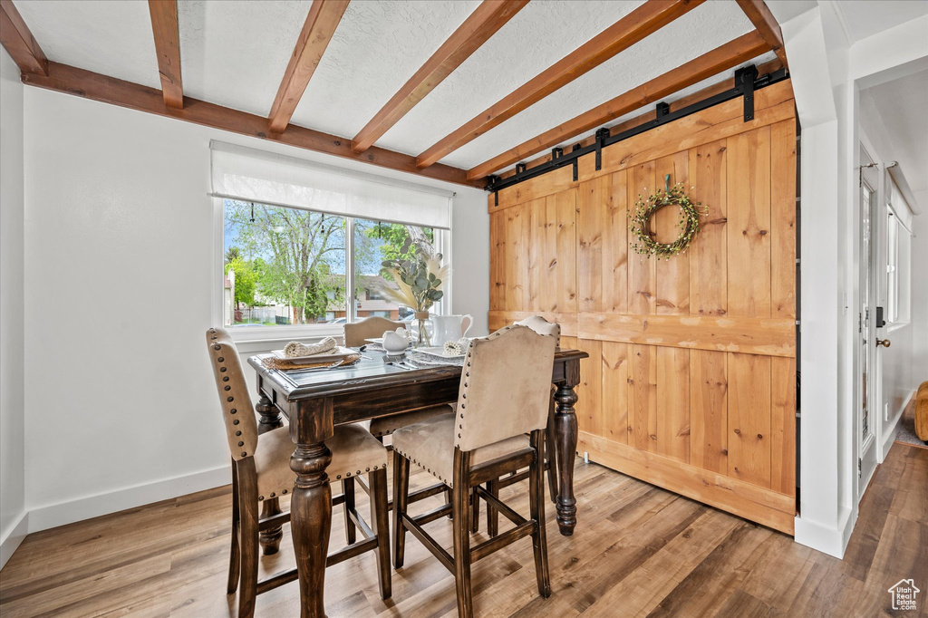Dining space featuring beamed ceiling, wood finished floors, baseboards, and a barn door