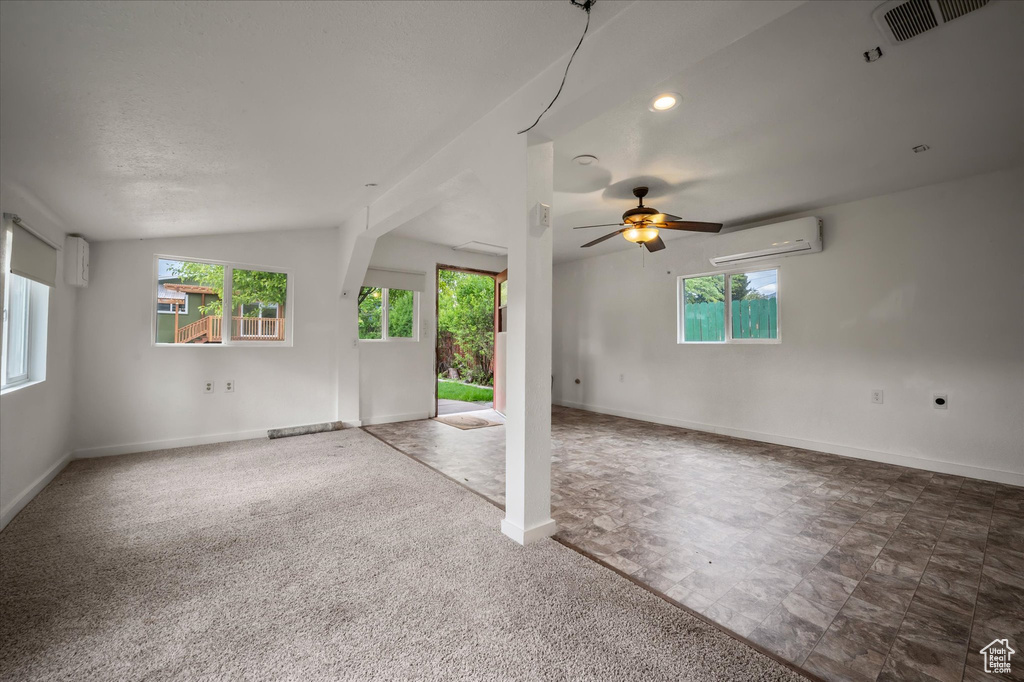Carpeted spare room featuring a wall unit AC, plenty of natural light, vaulted ceiling, ceiling fan, and baseboards