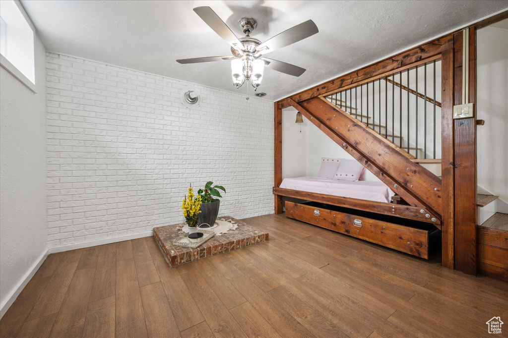 Interior space featuring brick wall, stairs, a ceiling fan, hardwood / wood-style flooring, and baseboards