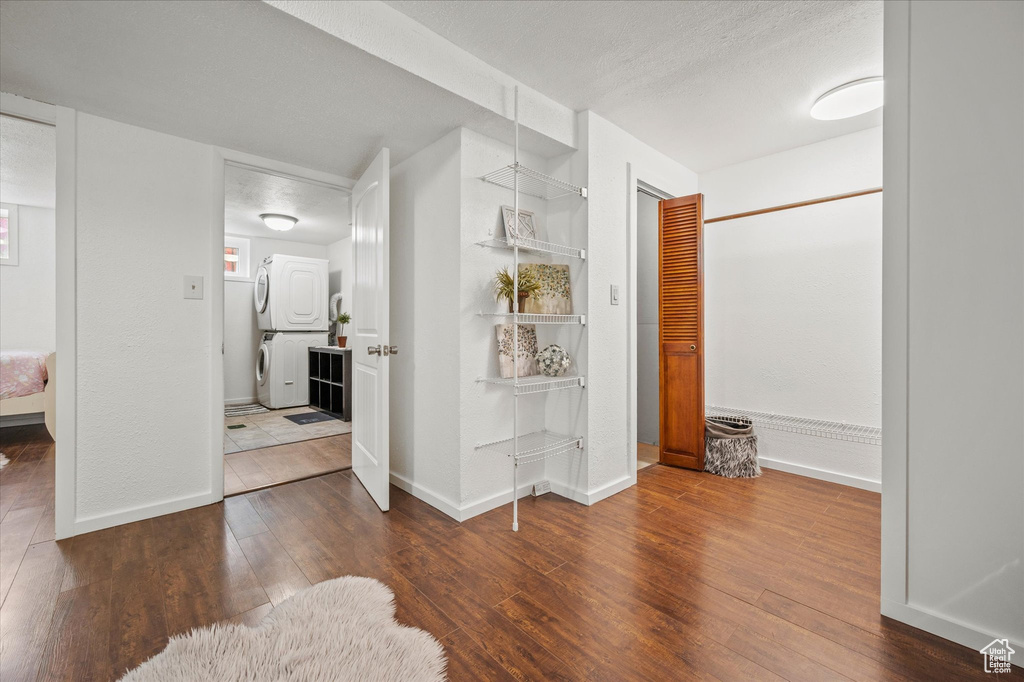Corridor featuring stacked washer and clothes dryer, hardwood / wood-style flooring, and baseboards