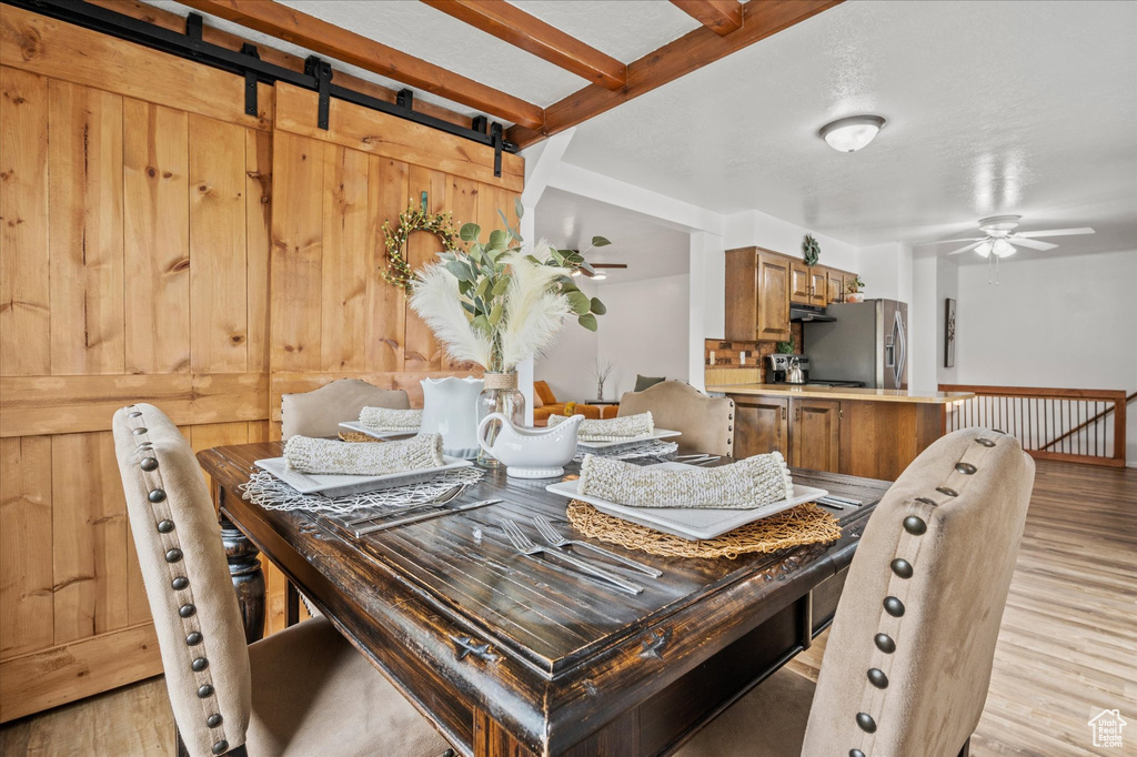 Dining space with light wood-style floors, ceiling fan, and a barn door